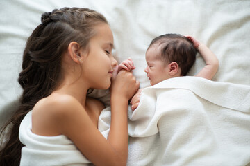 Obraz na płótnie Canvas Little girl sleeps with her new born baby sister at home. Cute children's portrait