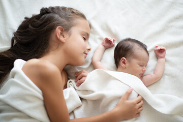 Little girl sleeps with her new born baby sister at home. Cute children's portrait