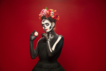Hurry up. Young girl like Santa Muerte Saint death or Sugar skull with bright make-up. Portrait isolated on red studio background with copyspace. Celebrating Halloween or Day of the dead. Sales