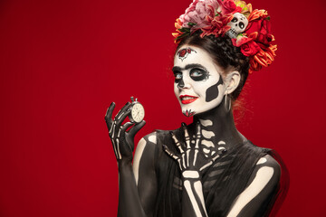 Hurry up. Young girl like Santa Muerte Saint death or Sugar skull with bright make-up. Portrait isolated on red studio background with copyspace. Celebrating Halloween or Day of the dead. Sales