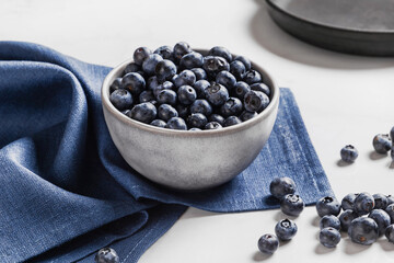 Bowl of fresh ripe blueberries on a blue fabric and white marble background. Healthy seasonal fruit. Organic food blueberries for healthy lifestyle and eating. Vegan, vegetarian concept. Rustic.