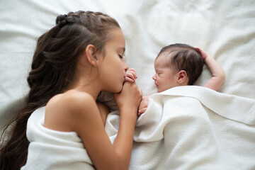 Little girl sleeps with her new born baby sister at home. Cute children's portrait