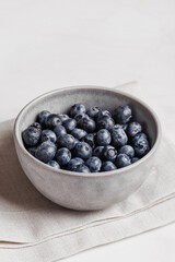 Bowl of fresh ripe blueberries on a white fabric and white marble background. Healthy seasonal fruit. Organic food blueberries for healthy lifestyle and eating. Vegan, vegetarian concept. Rustic.
