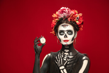 Hurry up. Young girl like Santa Muerte Saint death or Sugar skull with bright make-up. Portrait isolated on red studio background with copyspace. Celebrating Halloween or Day of the dead. Sales