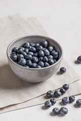 Bowl of fresh ripe blueberries on a white fabric and white marble background. Healthy seasonal fruit. Organic food blueberries for healthy lifestyle and eating. Vegan, vegetarian concept. Rustic.