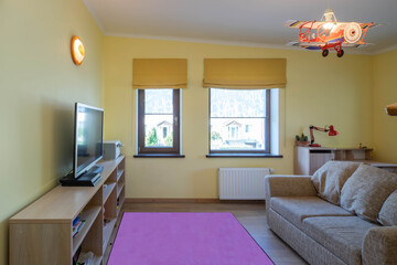 Contemporary interior in yellow tones of kid`s room with furniture in modern flat. Couch and TV.