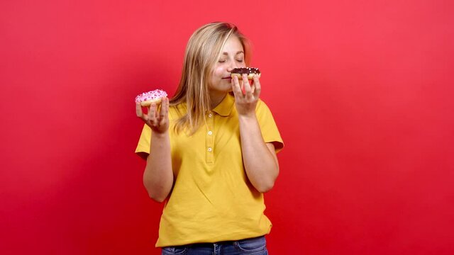 Pretty, fat girl in a yellow T-shirt holding two donuts in her hand. Pink donut and one with dark chocolate. diet. Fast food fod to fon.draw in interior studio isolated on red background.
