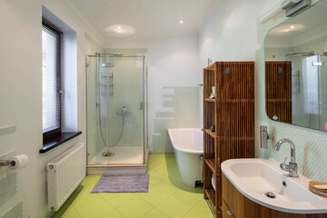 Contemporary interior of bathroom in private house. Bath and glass shower cabin. Wooden bamboo shelf.