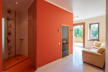 Modern interior of hall in luxury private house. Cozy couch. Shower cabin. Red wall.