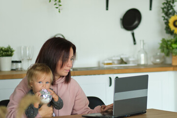 mom working remotely on laptop while taking care of her baby. Young mother on maternity leave...