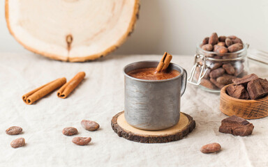 Fototapeta na wymiar Hot chocolate in a metal mug with a cinnamon stick on the tablecloth. Copy space