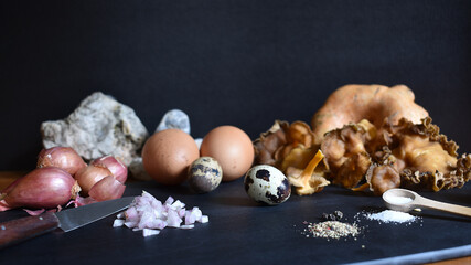 Zutaten für Rührei mit Pilzen auf schwarzem Brett vor schwarzem Hintergrund mit Eiern,...