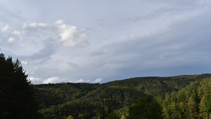 Wolken und Sonne wechseln sich ab &uuml;ber H&uuml;gelland mit Wald