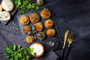  Baked stuffed mushrooms on black slate plate with sauce top view, free space for text