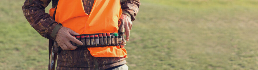 Duck hunter with shotgun walking through a meadow.