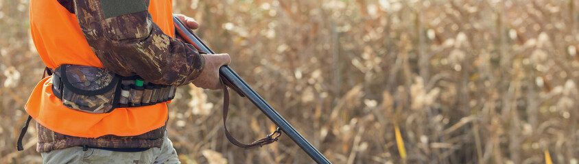 Duck hunter with shotgun walking through a meadow.
