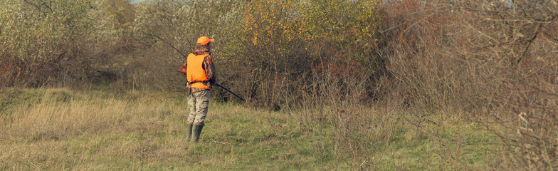 Duck hunter with shotgun walking through a meadow.