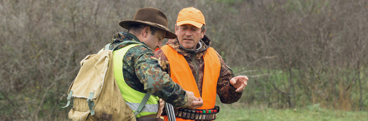 A mans with a gun in his hands and an orange vest on a pheasant hunt in a wooded area in cloudy...