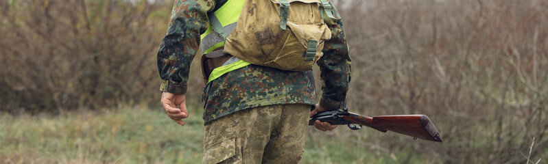 Duck hunter with shotgun walking through a meadow.