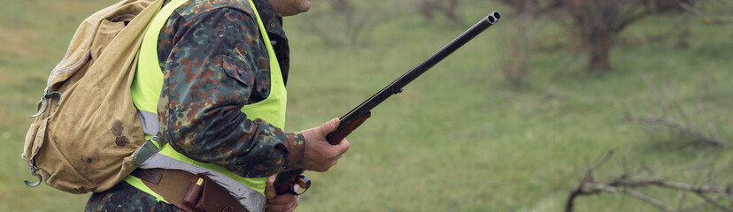 Duck hunter with shotgun walking through a meadow.