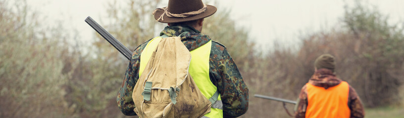 A mans with a gun in his hands and an orange vest on a pheasant hunt in a wooded area in cloudy...