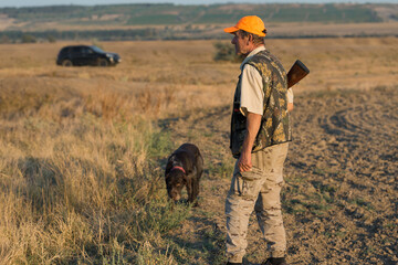 Duck hunter with shotgun walking through a meadow. .Rear view of a man with a weapon in his hands.