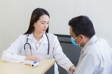 Asian beautiful young woman doctor talking with a man patient about his pain and symptom while they put on a face mask to prevent Coronavirus disease in hospital.