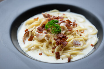 Spaghetti carbonara with a white sauce and on top with crispy bacon and parsley.