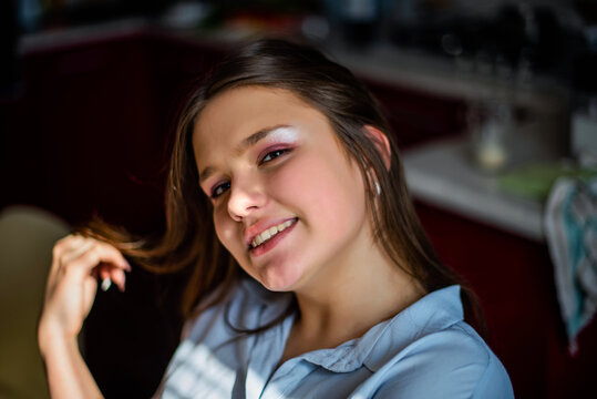 Fashion lifestyle image of pretty teenage young woman sitting in kitchen.