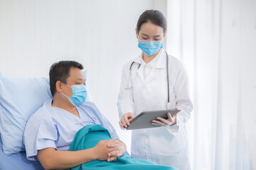 Asian woman doctor talking with a man patient who he is on bed about his pain and symptom in hospital. They wear a medical face mask to protect respiration system (Covid-19).