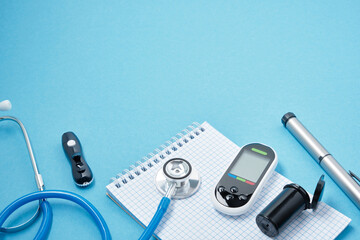 clean block with spring, stethoscope, glucose meter, lancet and syringe pen with insulin on a blue background, daibet day concept, diabetes diagnosis