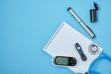 clean block with spring, stethoscope, glucose meter, lancet and syringe pen with insulin on a blue...