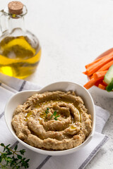 hummus sauce in a bowl, sesame seeds, olive oil, cucumber and carrots on a light background