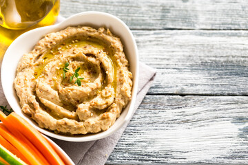 hummus sauce in a bowl, sesame seeds, olive oil, cucumber and carrots on a light background