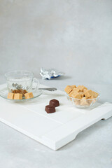 sweet still life of brown cane sugar in a sugar bowl and chocolates on  white tray. blurred