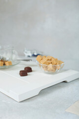 sweet still life of brown cane sugar in a sugar bowl and chocolates on a white tray. soft focus and highly blurred background. stylish background concept