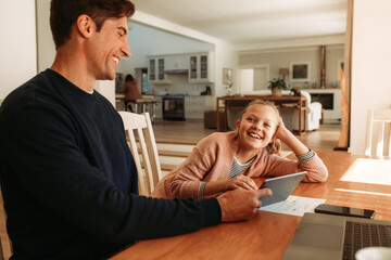 Smiling father and daughter at home with digital tablet