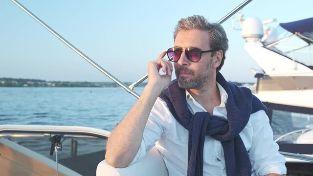 Handsome man wearing sunglasses on the yacht. Portrait of successful man on sailing boat at sunset in marina.
