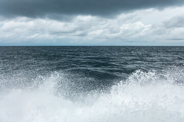 Grey ocean water splashes under cloudy grey sky shot from a speed boat on Maldive islands 