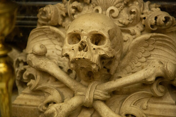 Detalle mortuorio tallado en piedra de talla de calavera y femur cruzados