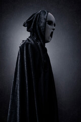 Naklejka premium Ghostly figure in hooded cloak in the dark