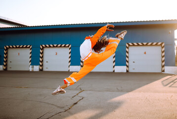 Young sporty woman dancer dancing in the street at sunset. African American woman in an orange suit showing some moves. Sport, dancing and urban culture concept.