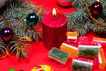 Marmalade on a red background with a burning candle. Banner for confectionery with Christmas decorations. Gifts for New Year 2021.