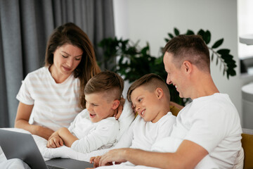 Beautiful parents with kids enjoying at home. Young family watching movie on lap top