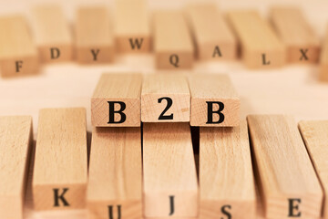 Word B2B Business to Business on wooden blocks beige background top view, scattered cubes around random letters