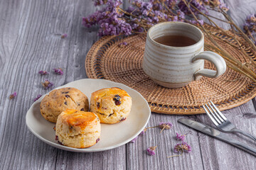 Close-up of traditional British scones and cookie with a tea cup on wooden table with flower blurred background. Space for text.