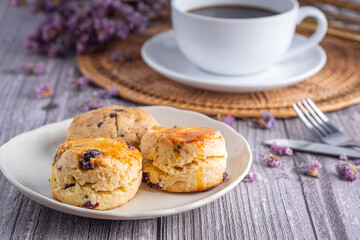 Close-up of traditional British scones and cookie with a white coffee cup on wooden table with flower blurred background. Space for text.