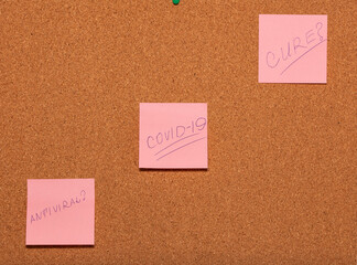 Covid-19, Antiviral?, Cure? handwritten on three pink stickers across a cork notice-board.
