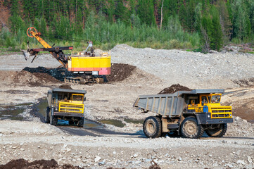 Excavator loads mountain soil into the body of a mining dump truck and then transports the load. Extraction of minerals in the mountainous region of Eastern Siberia © Letopisec