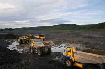 Loading of mountain soil into the body of a mining dump truck using a wheel loader, and further transportation of the cargo. Extraction of minerals in the mountainous region of Eastern Siberia © Letopisec